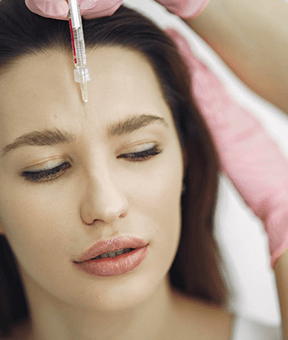 A close-up of a woman receiving a facial serum treatment with a dropper.