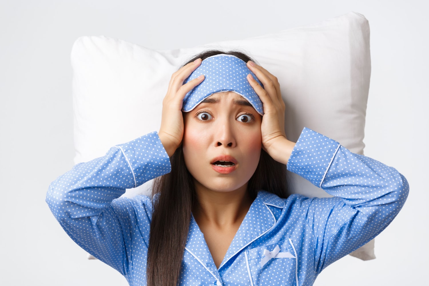 Woman in blue pajamas looking distressed while holding her head.